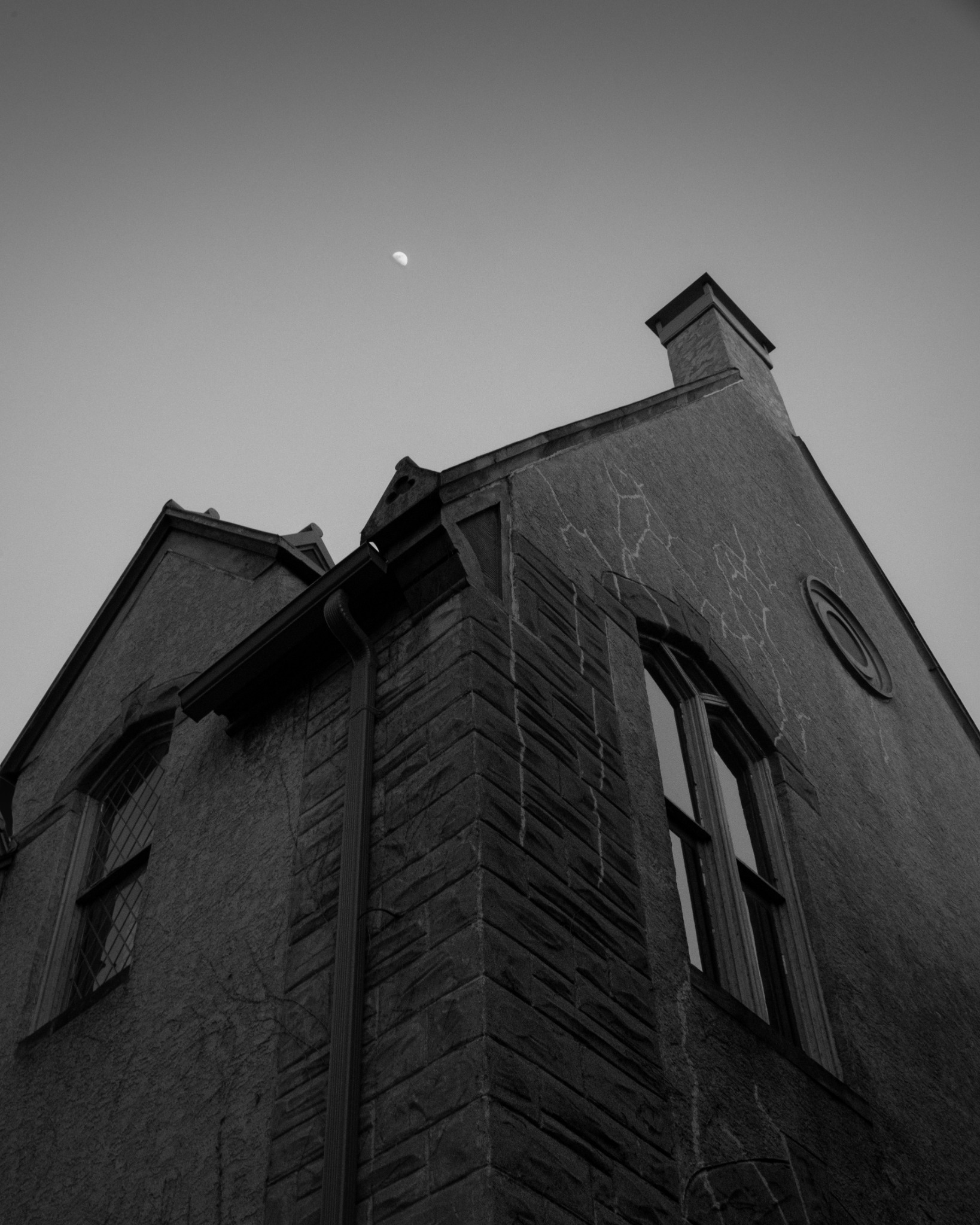 A black-and-white view looks upward along an old church wall toward the moon.